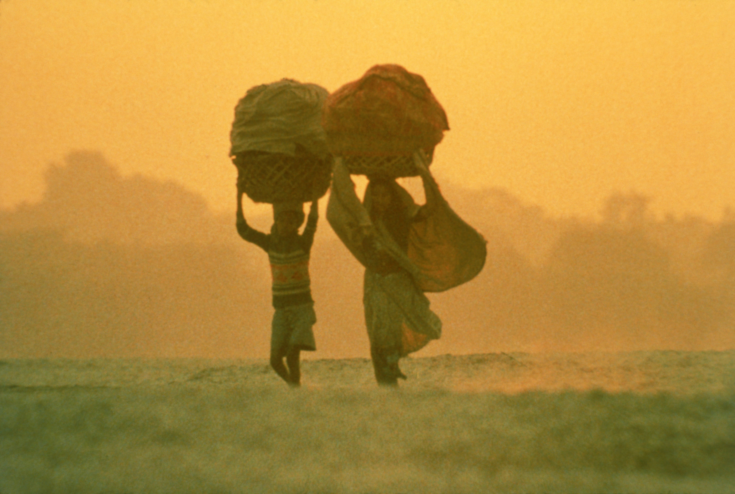 Kadr filmu "Powaqqatsi", przedstawiający kobietę i chłopca niosących kosze na głowie, pośród pustynnego terenu.